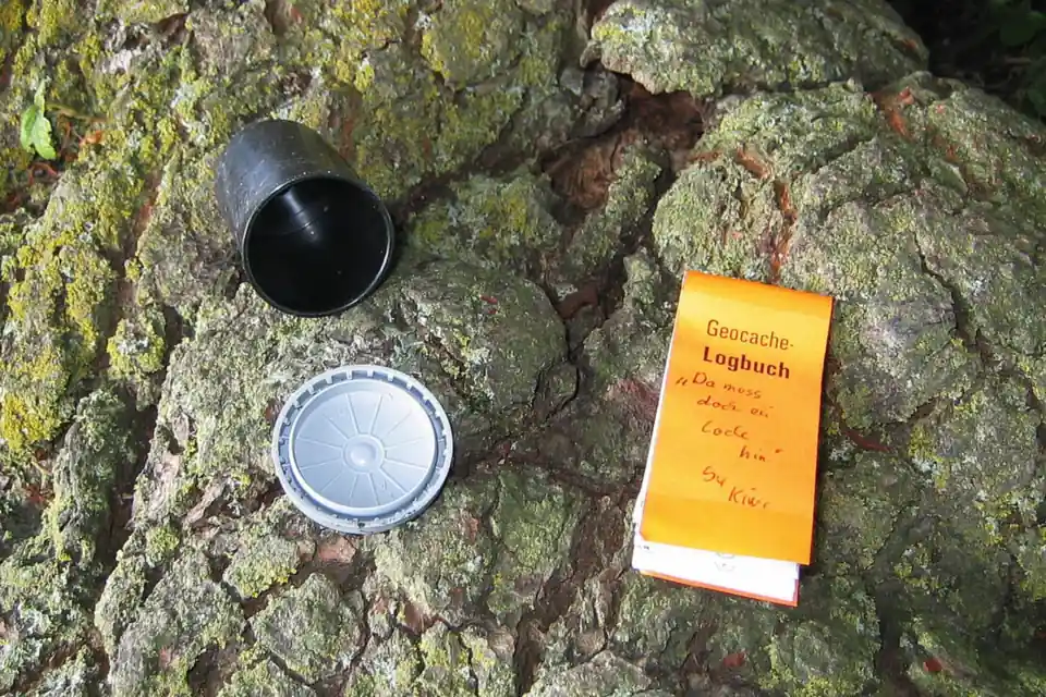 Kleiner Geocache aus einer Filmdose mit Logbuch, abgelegt am Boden